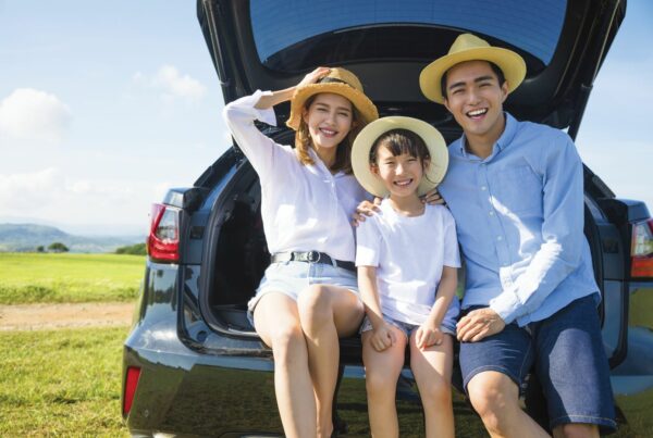 an happy asian family sitting at the back of a SUV smiling with hats.
