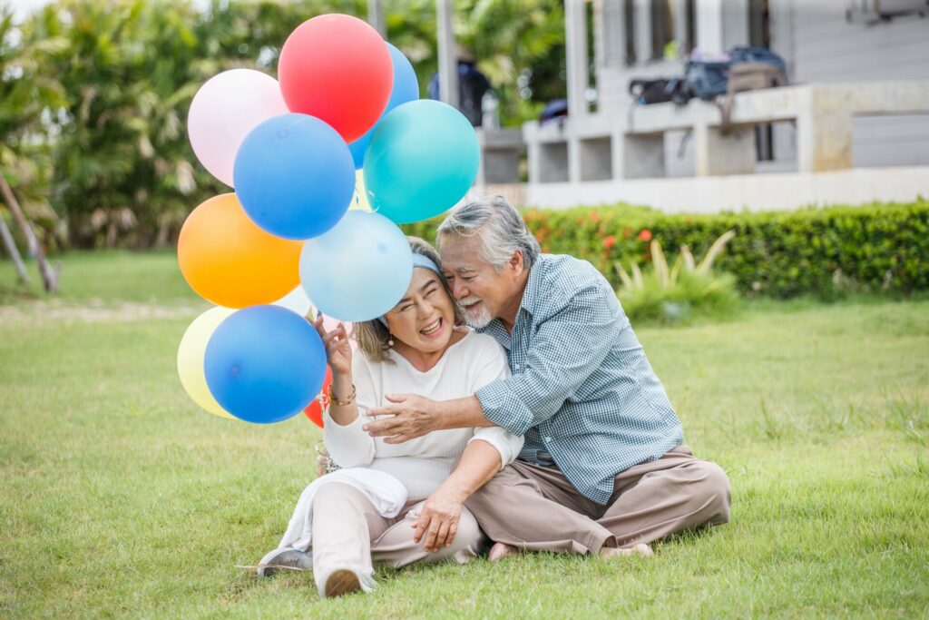 senior couple happily sit on grass with big balloon and big smile hugging each other.