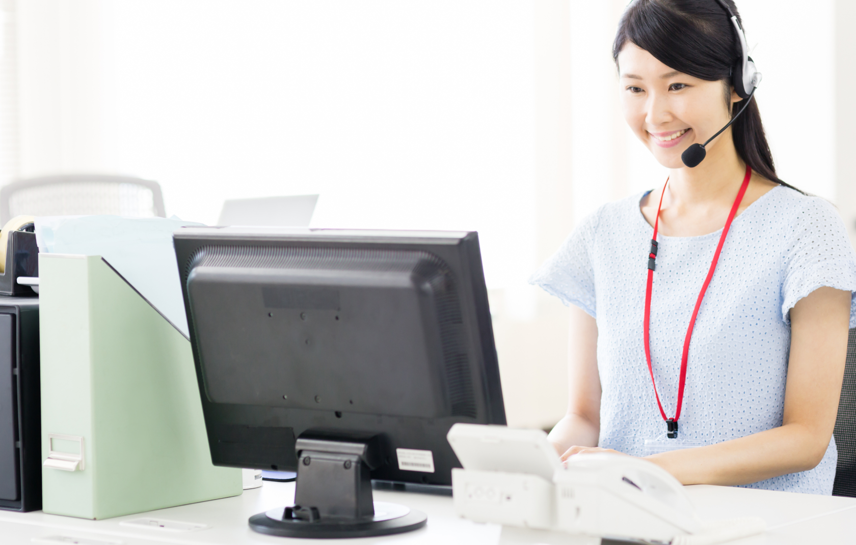 smiling receptionist wearing headset and sitting in front of a computer screen