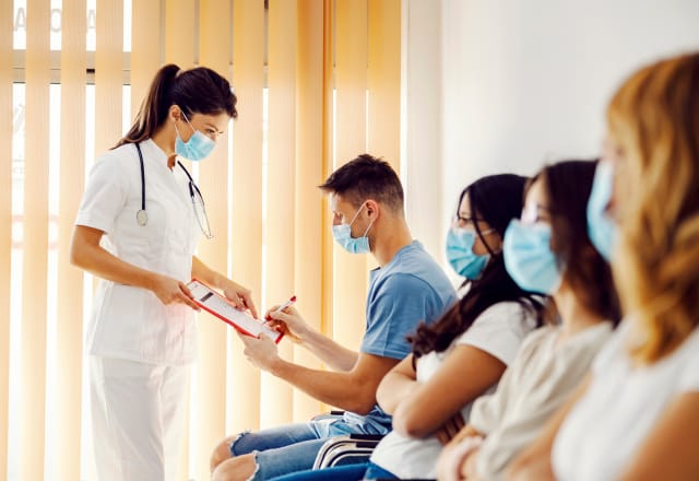 young female nurse with clipboard amongst patients in wating room